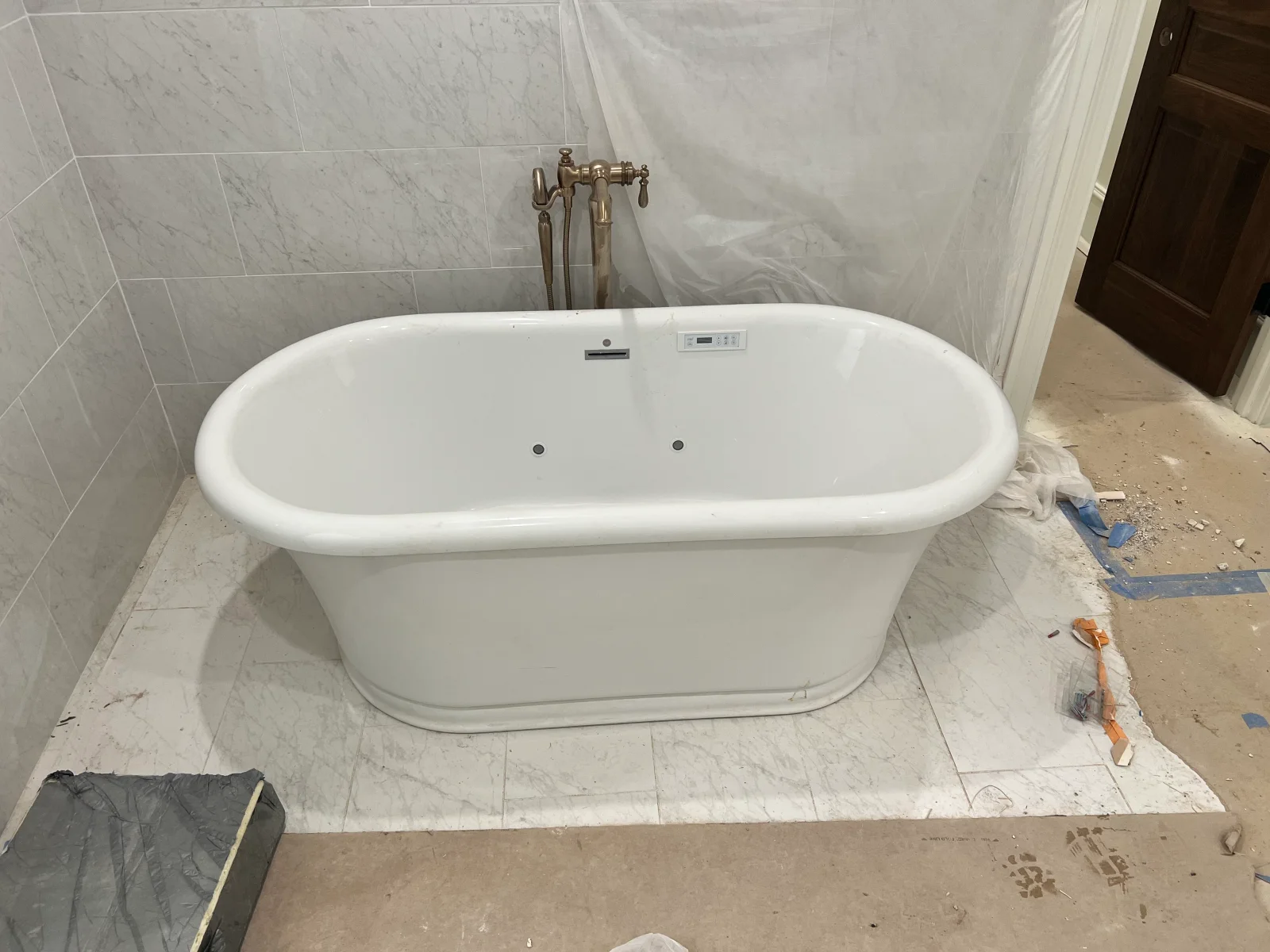 White freestanding soaking tub with marble tile surround and deck-mounted brass filler fixture