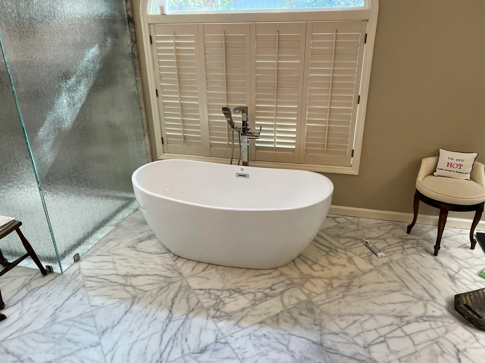 White freestanding soaking tub with floor-mounted filler on marble tile flooring
