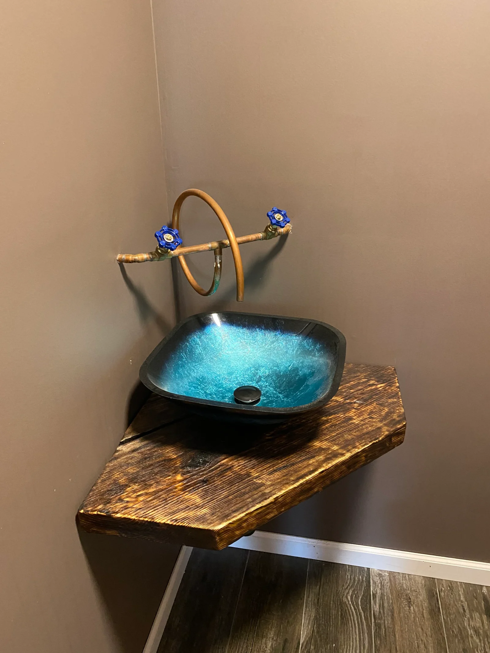Turquoise glass vessel sink with copper curved faucet and blue ball valves on wood vanity
